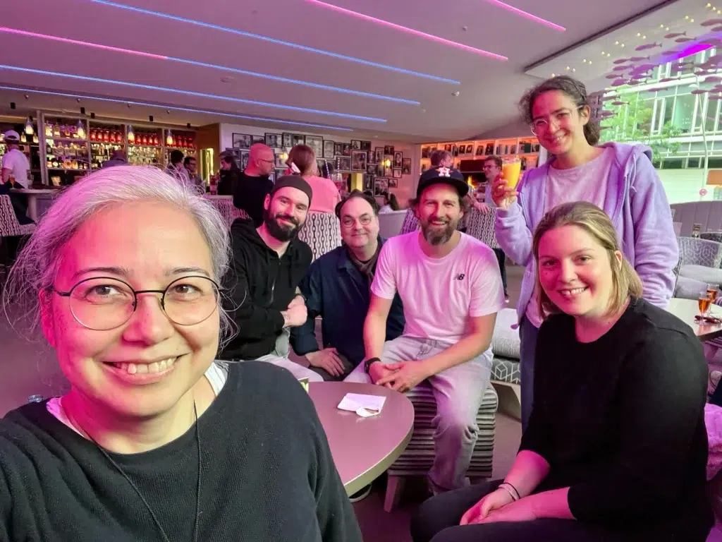 Das Sterntaucher Team sitzt in einer Lounge und schautfröhlich in die Kamera. Im Hintergrund ist eine Bar sowie verschiedene Tische und Sitzgelegenheiten, Bilderrahmen an der Wand sowie an der Decke schwebende Fische zu sehen.