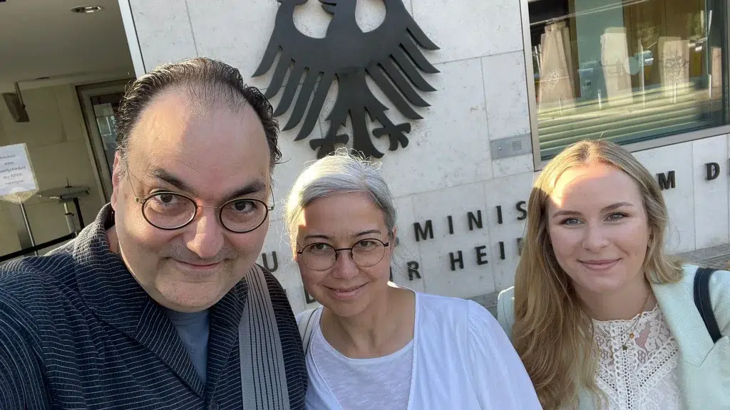 Drei Personen posieren für ein Selfie vor dem Gebäude des Bundesministerium des Innern und für Heimat in Berlin.